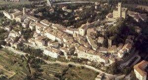 Veduta aerea di una storica cittadina collinare con edifici in pietra e un'imponente torre campanaria.