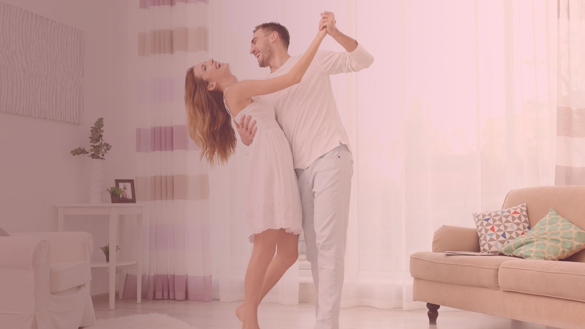 A couple dances in a light-filled living room. The woman leans back, smiling, as the man holds her.