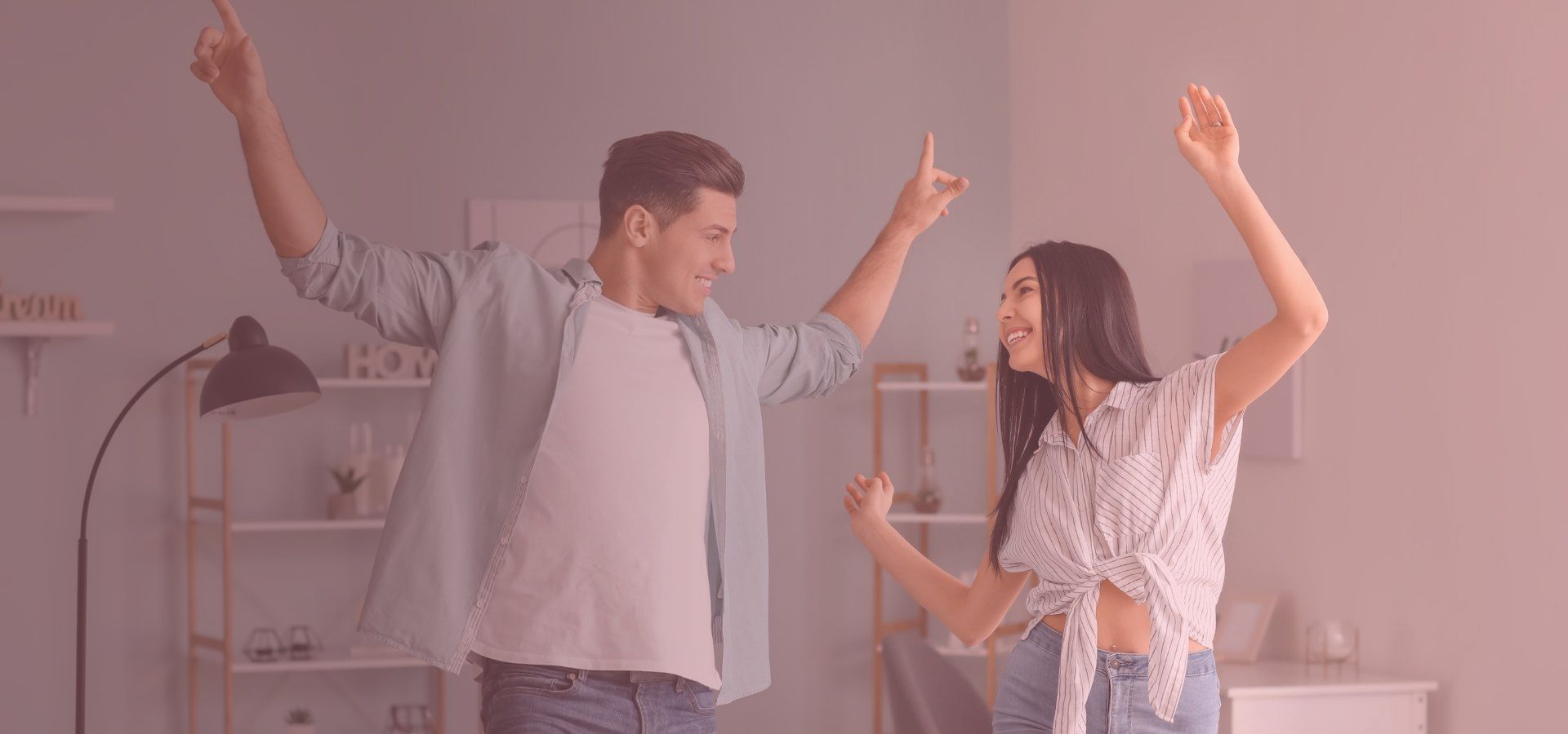 A couple dances in a room with joy, both pointing upwards.