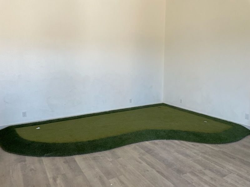 Small indoor room with a green putting turf mat on the floor