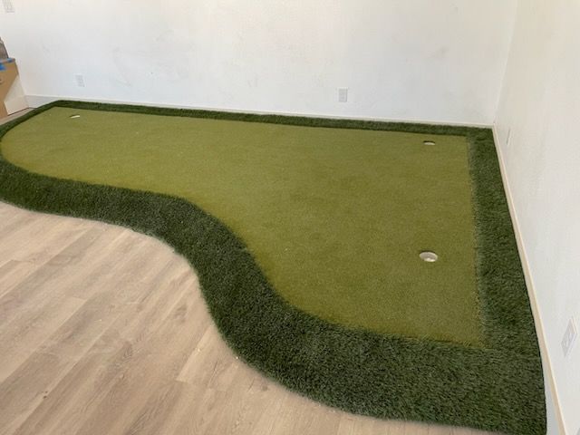 Green artificial turf corner rug in an empty room with wood flooring and white walls