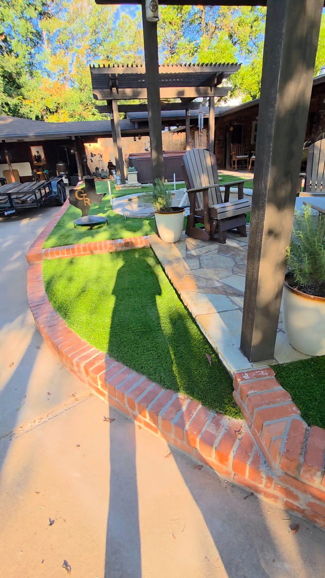 Sunlit courtyard with brick walkway, green turf, outdoor tables, and pergola between buildings.