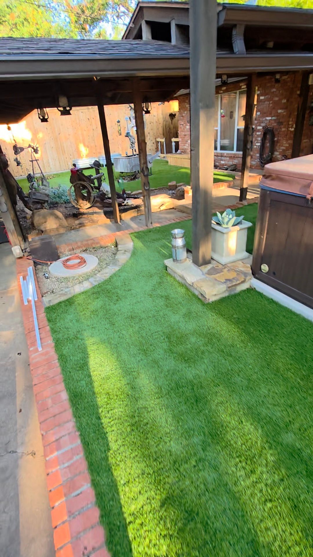 Backyard patio with green lawn, brick path, covered seating area, and potted plants