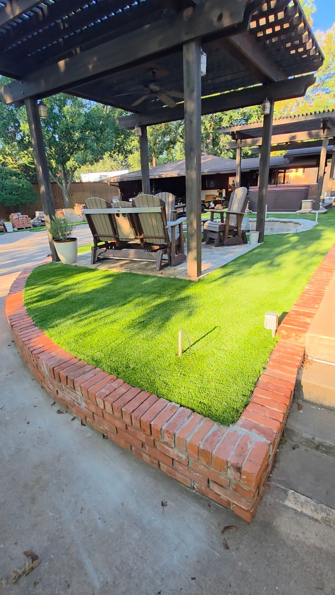 Outdoor patio seating under a black canopy, with tables and chairs on a brick-bordered patch of grass.