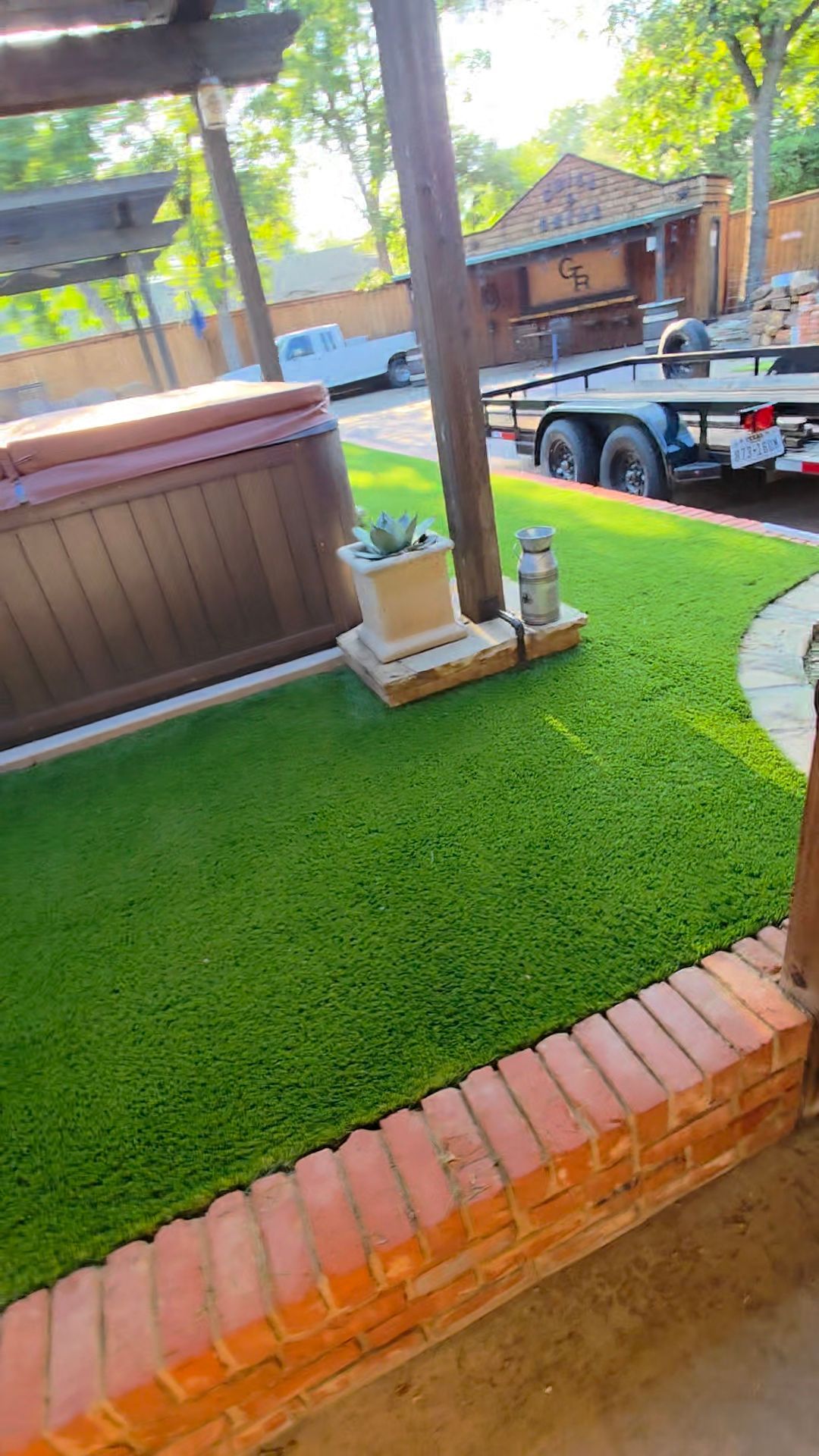 Patio with green turf, brick edging, hot tub, and a parked truck in the driveway.