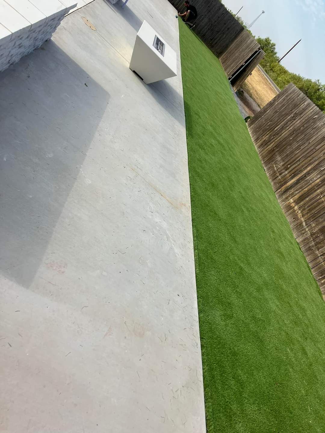 Concrete patio beside green lawn and wooden fence, with a small white ramp in the distance.