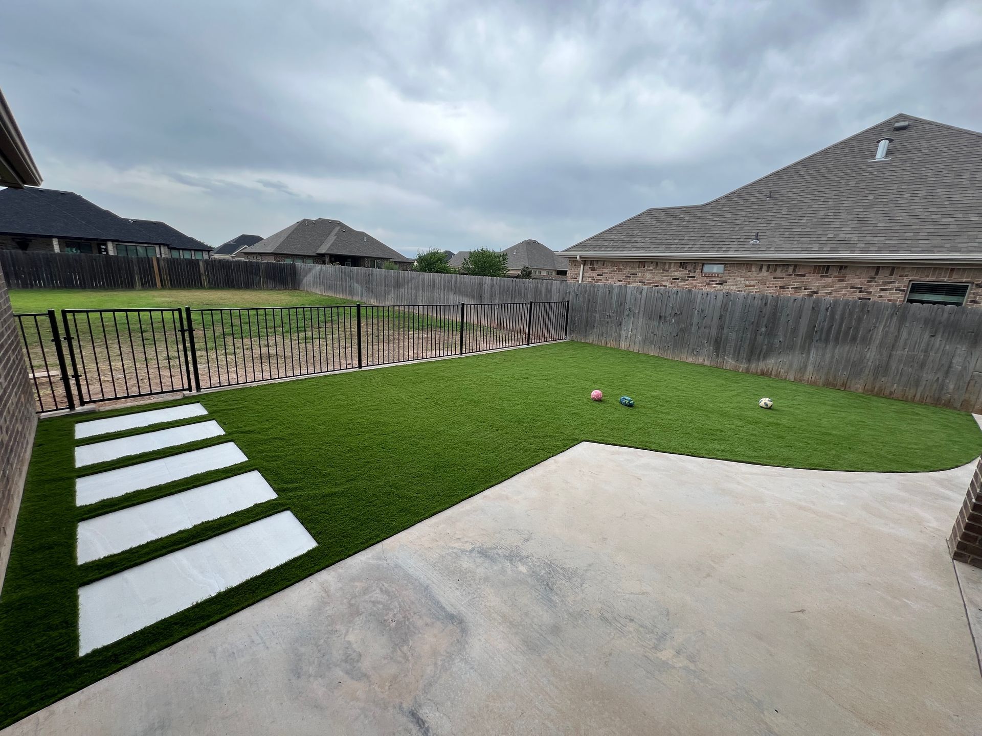 Backyard with artificial turf, stepping stones, and a concrete patio under a cloudy sky