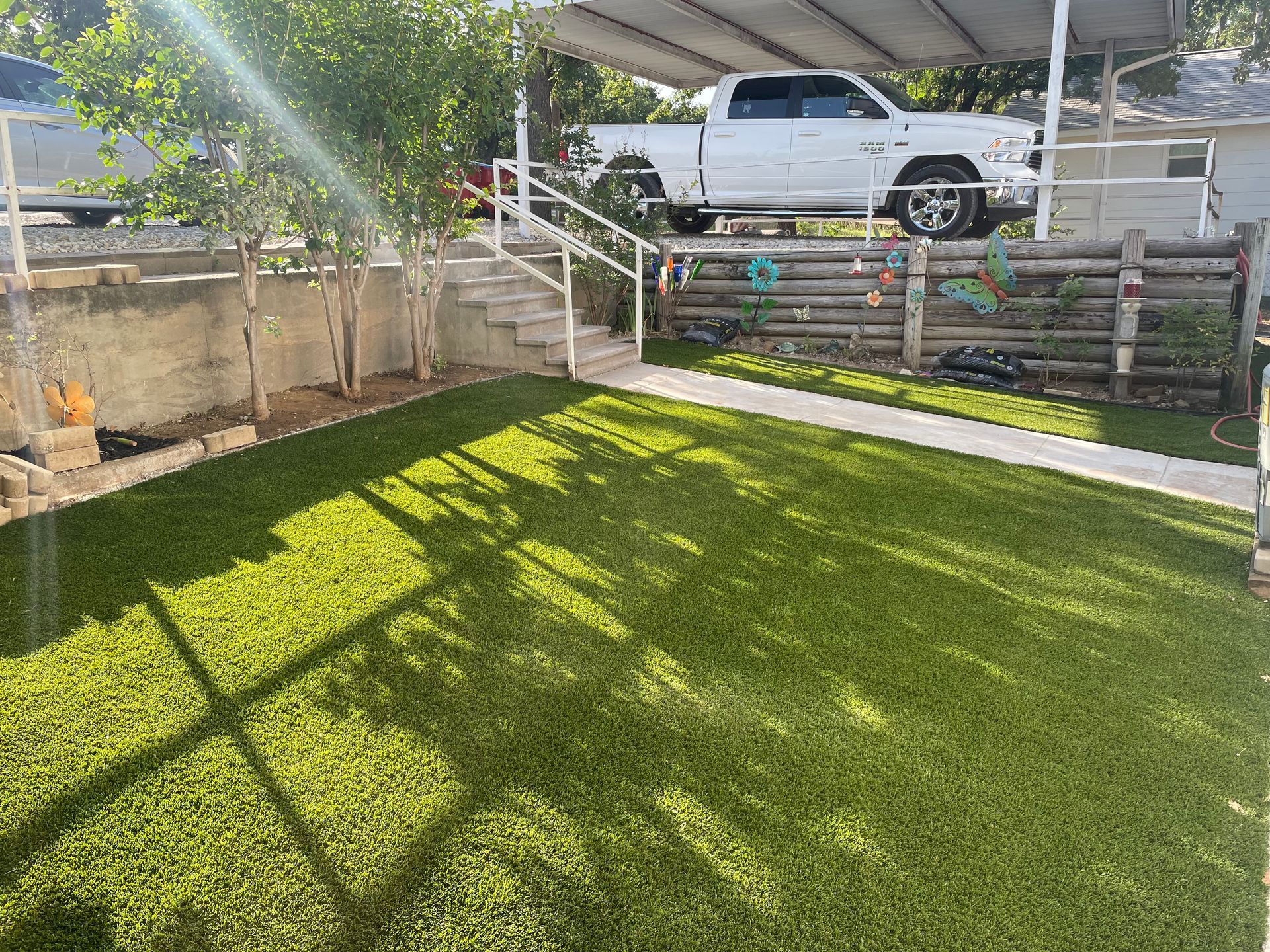 Sunny backyard with green lawn, patio steps, and a white truck parked above the yard.