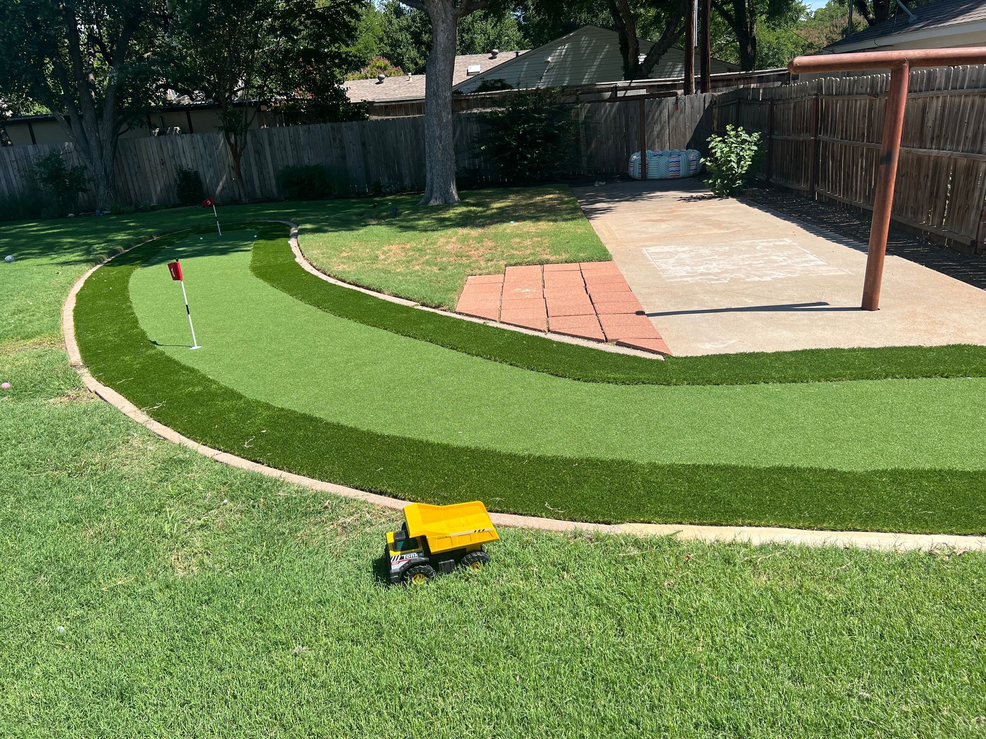 Backyard mini golf green with curved putting lane, flagstick, and a yellow line-marking machine.