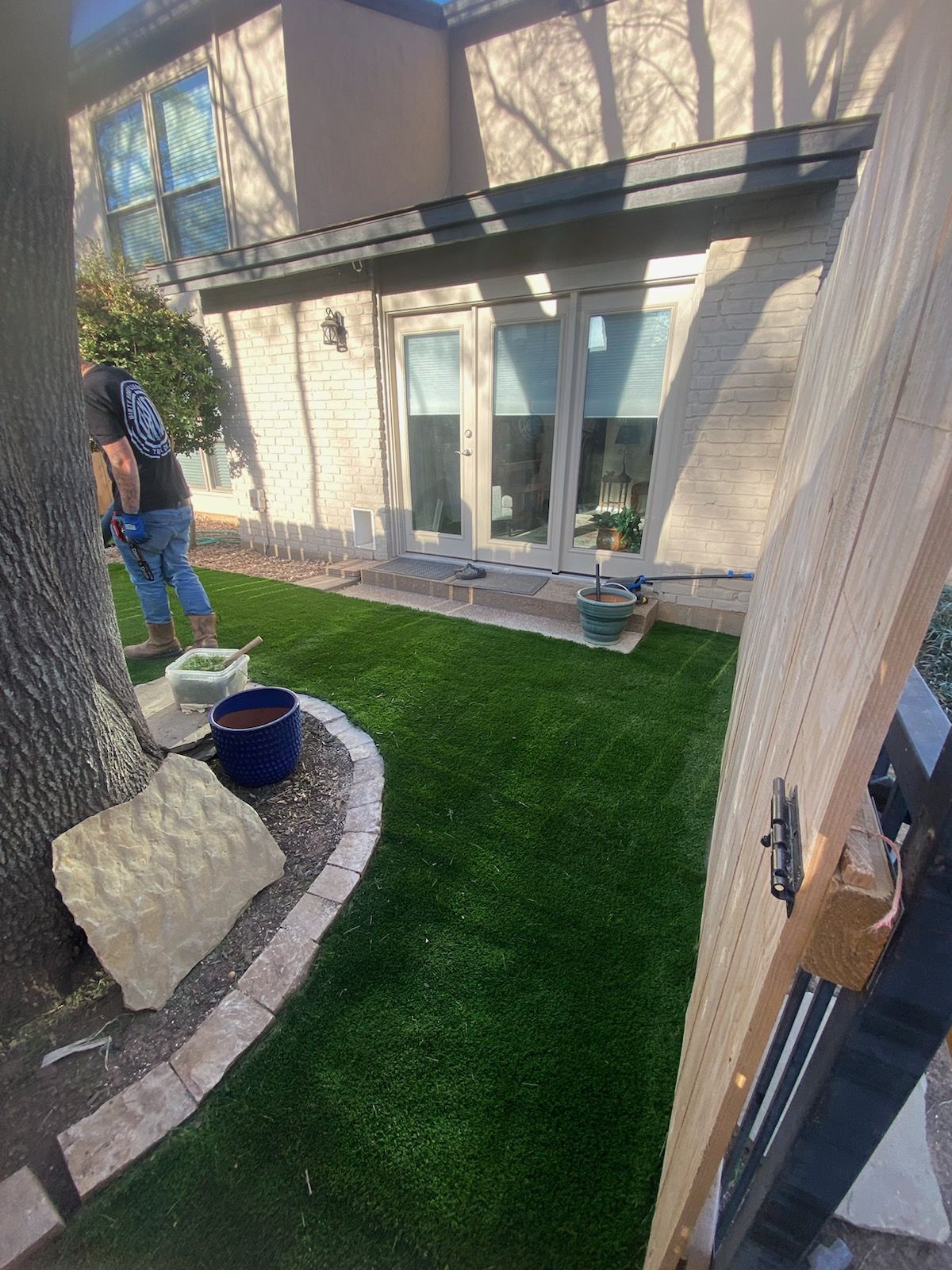 Backyard patio with artificial turf, two people on the left, and sliding glass doors on a tan house
