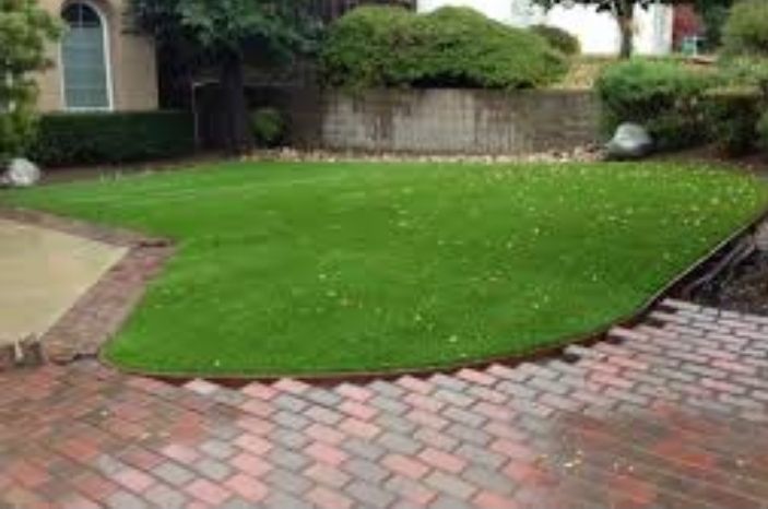 Brick-paved driveway surrounding a neatly landscaped green lawn with shrubs and house exterior in the background