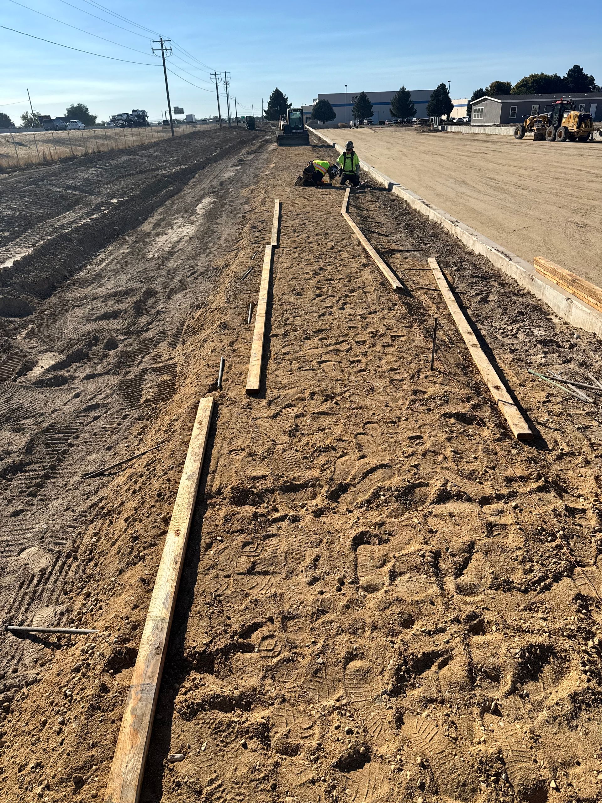 Construction site with wooden guides in the dirt, equipment and buildings in the background.