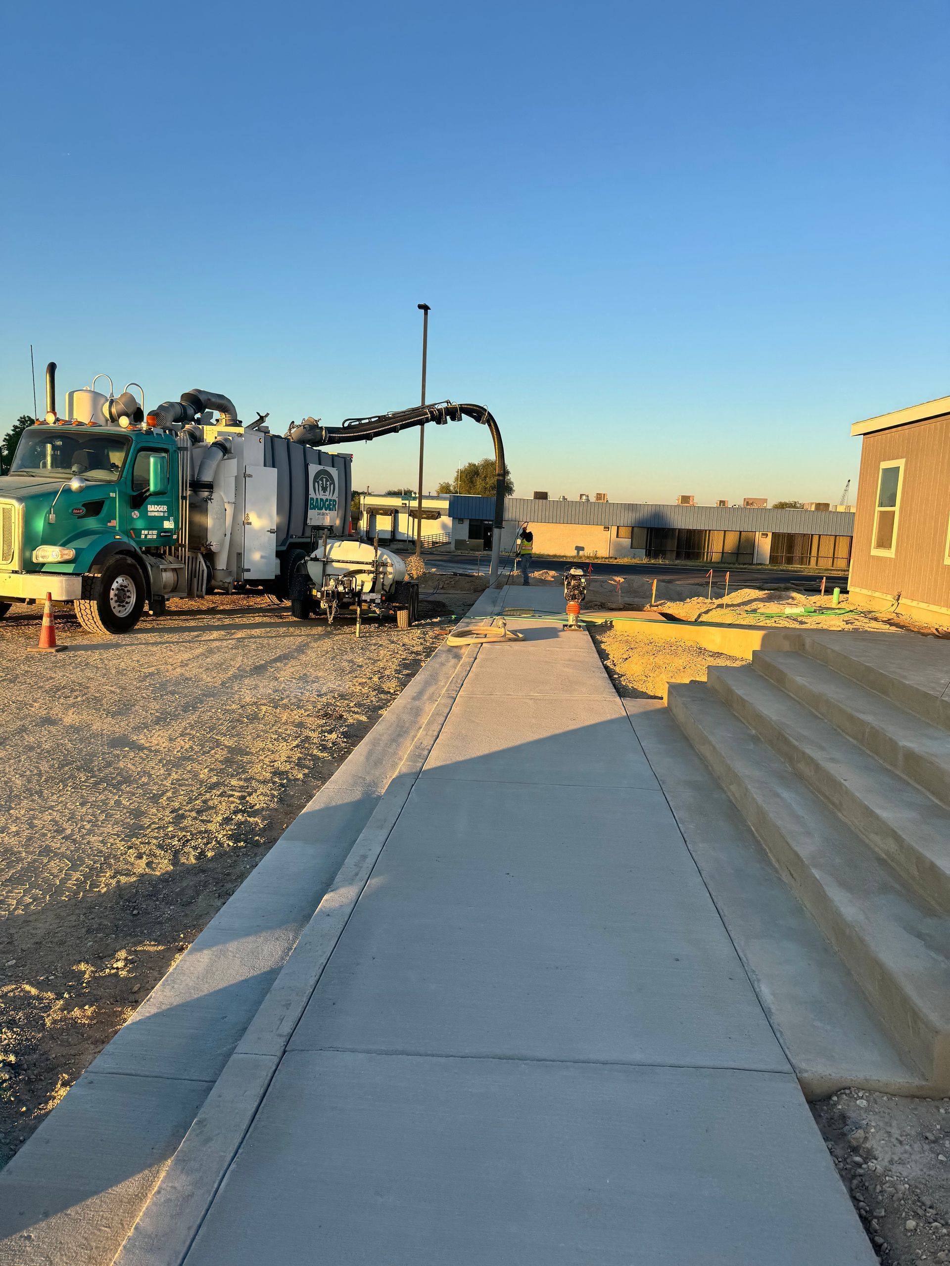 Cement truck pouring concrete on a sidewalk next to a building under construction.
