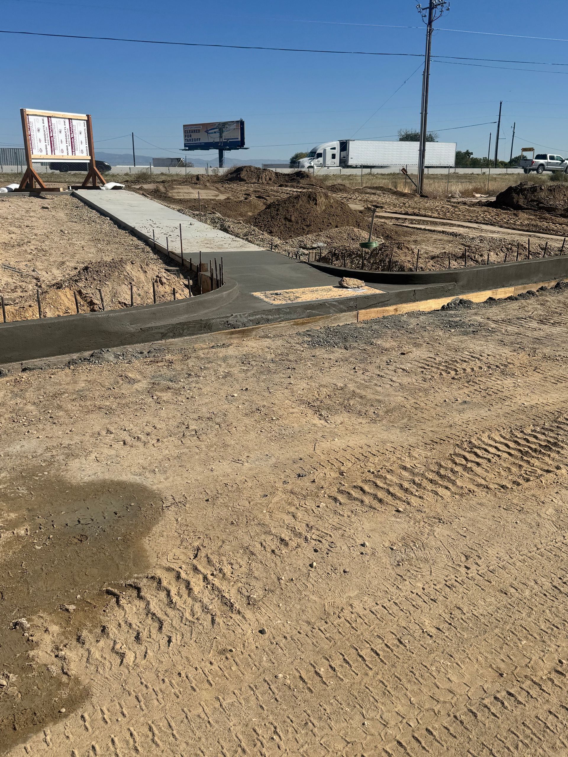 Construction site with a concrete path, soil, and a sign.