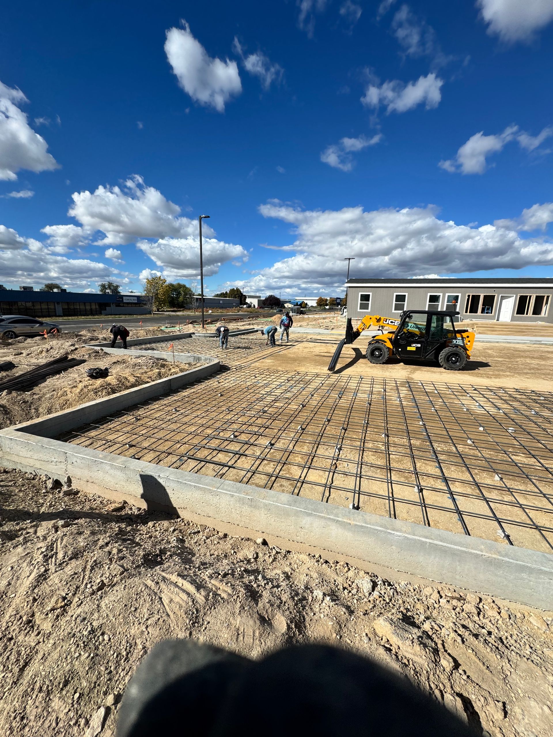 Construction site; workers, equipment pouring concrete. Blue sky with clouds.