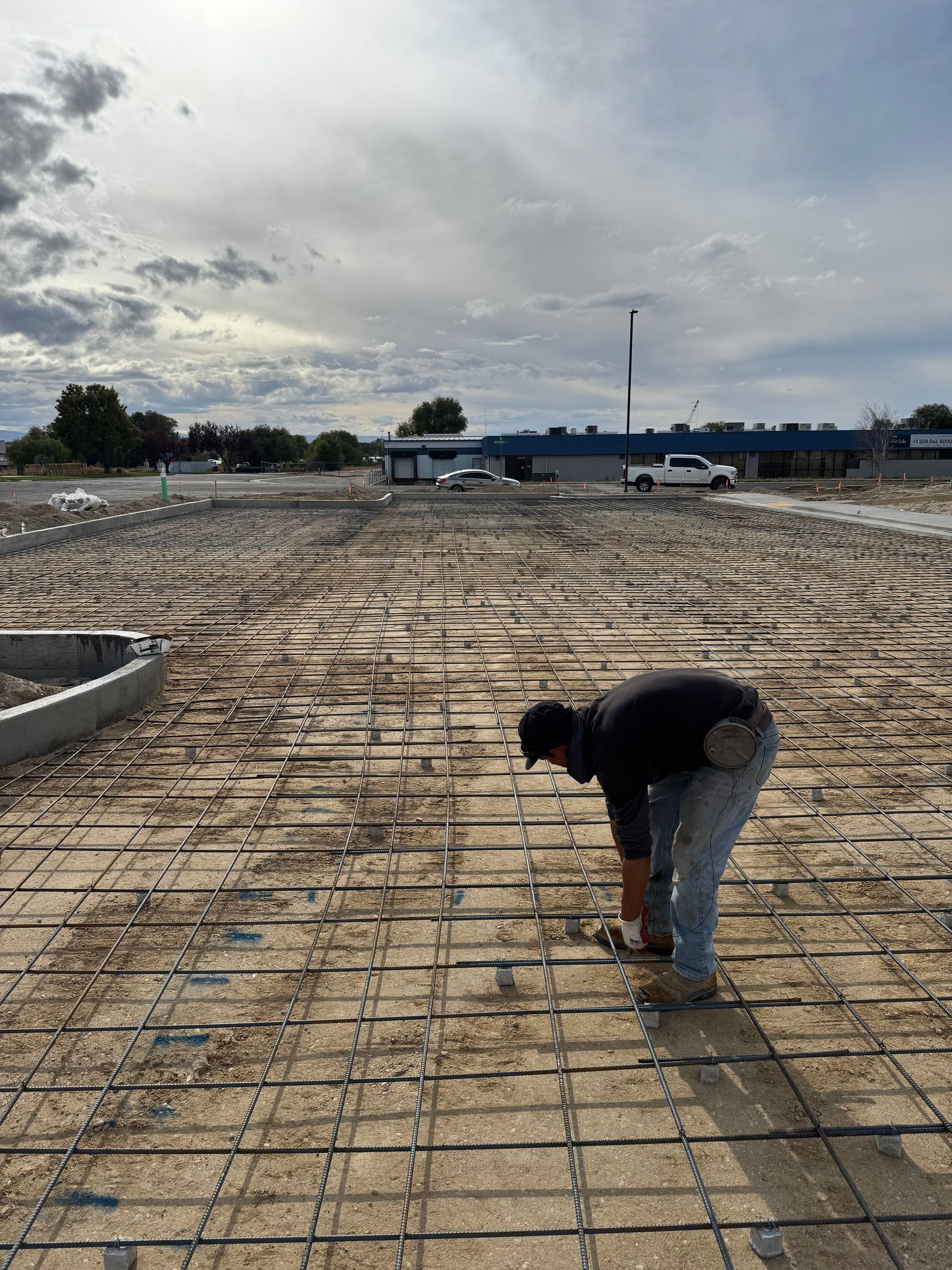 Construction worker bends over rebar, preparing concrete slab outdoors on a cloudy day.