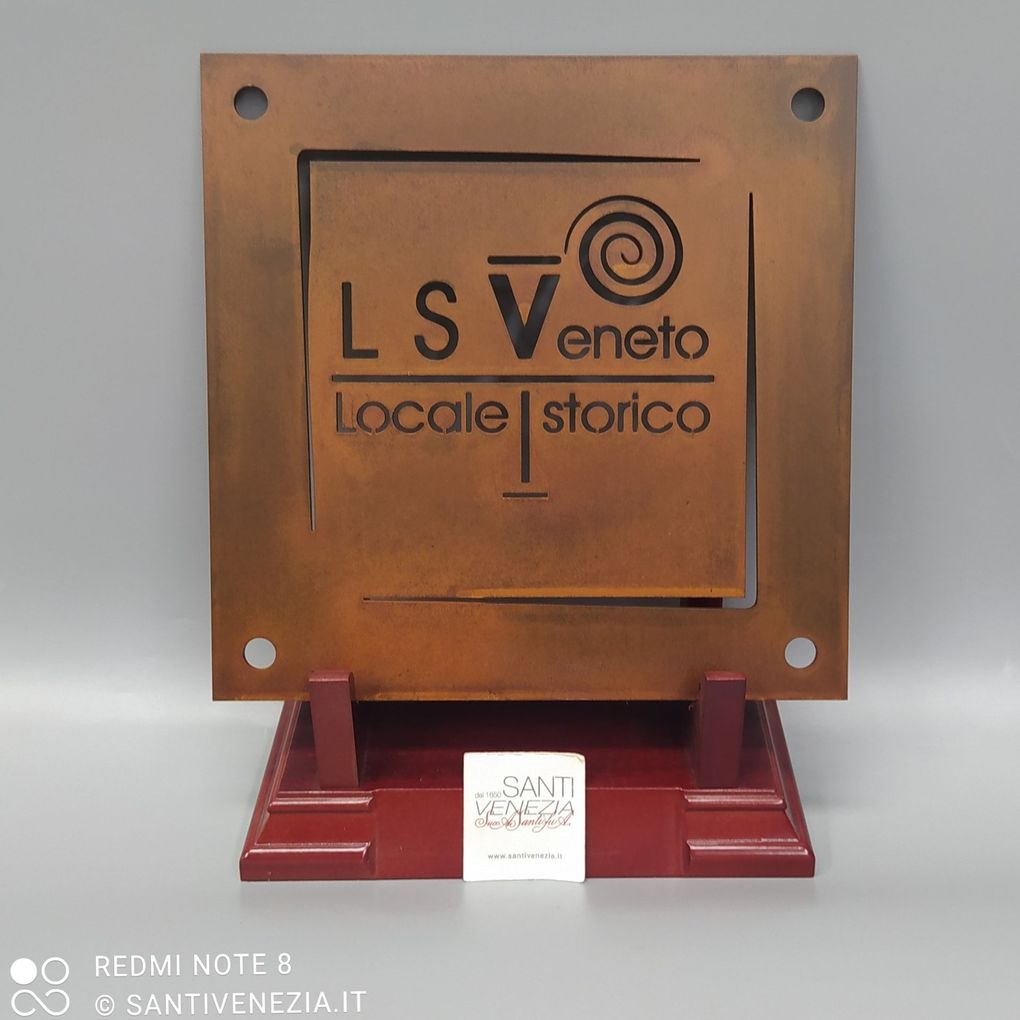 Una targa metallica quadrata color ruggine con il logo "LSV Veneto Locale Storico" montata su una base di legno rosso scuro.