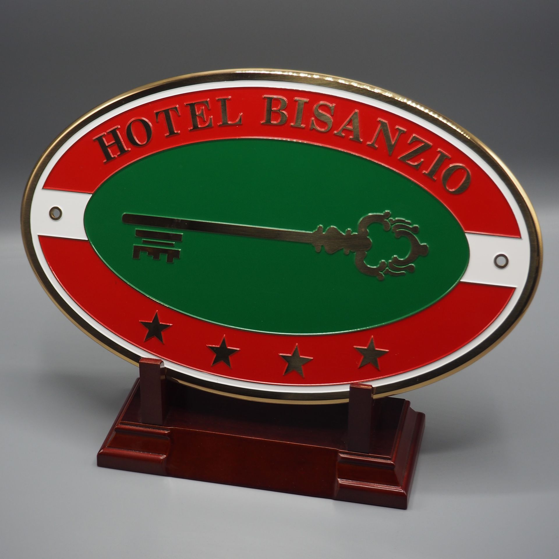 Targa ovale dell'Hotel Bisanzio a 4 stelle, con centro verde e chiave scheletro dorata, posta su un supporto in legno.