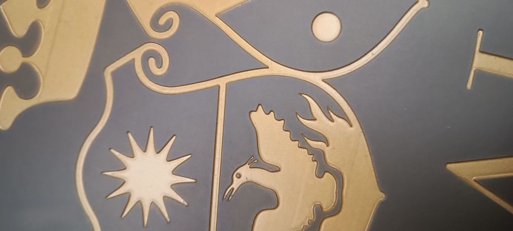Uno stemma dorato raffigurante una stella e un uccello, inciso su uno sfondo blu scuro con decorazioni a volute.