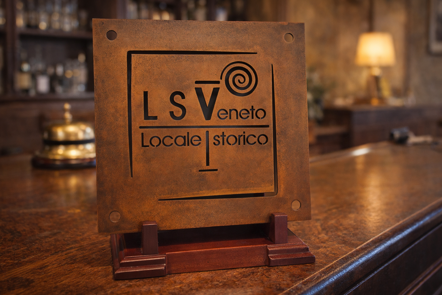 Una targa color bronzo su un supporto di legno reca la scritta "LSVeneto Locale Storico", posta su un bancone di un bar con uno sfondo sfocato.
