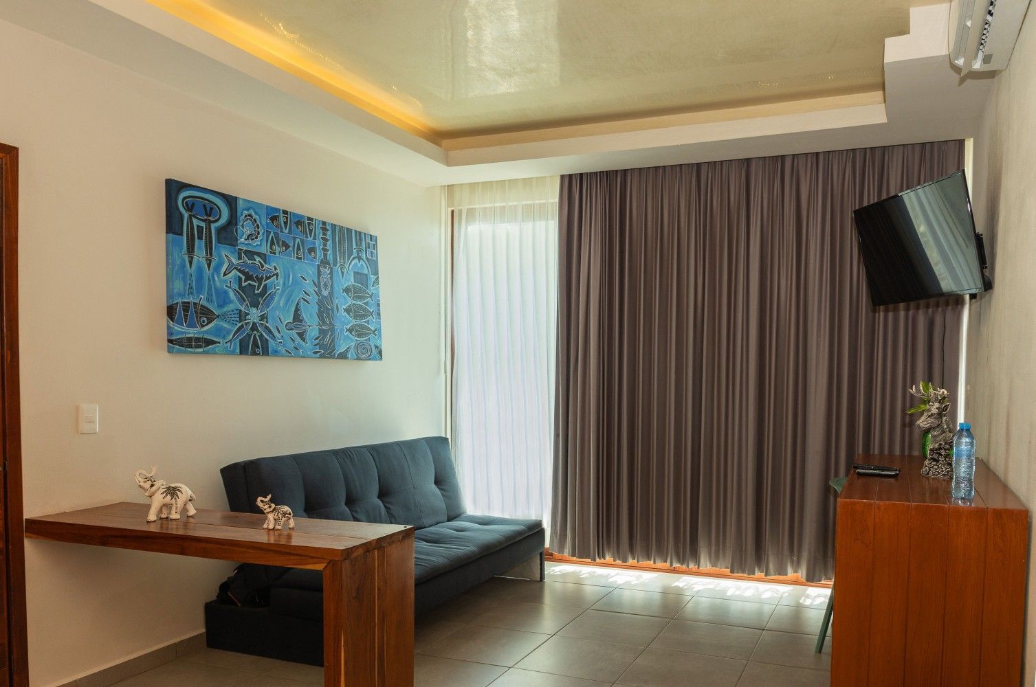 Sala de estar moderna con sofá gris, muebles de madera, cuadros en la pared y cortinas cerradas junto a la ventana.