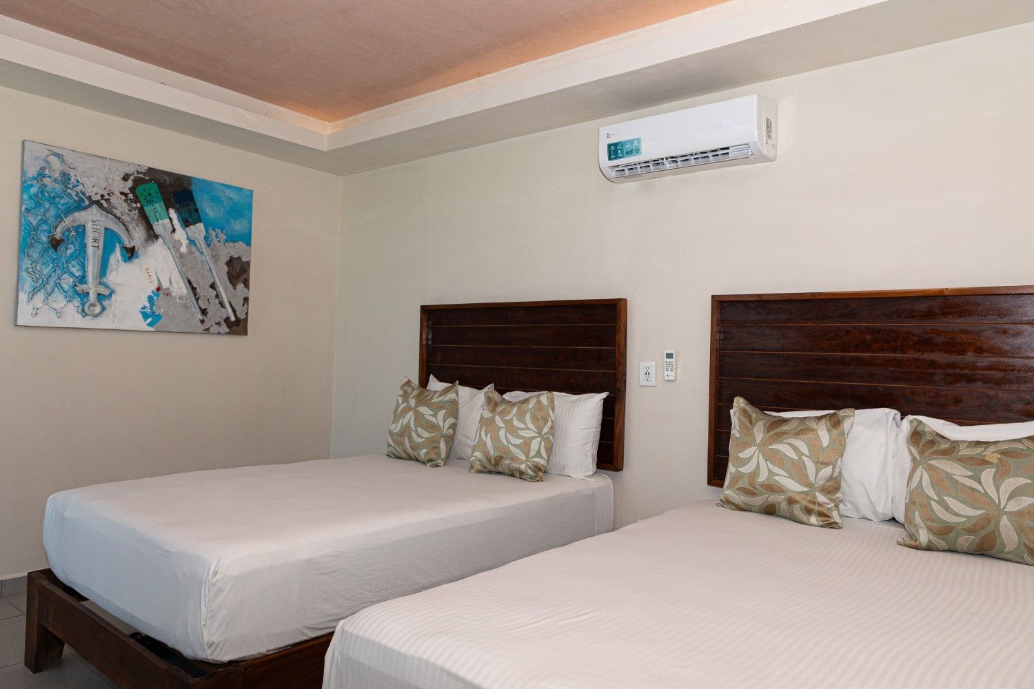 Dos camas bien hechas en una habitación de hotel de color beige con un cuadro en la pared y aire acondicionado.