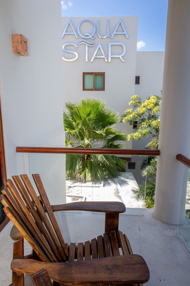 Vista desde el balcón de un patio con un letrero de AQUA STAR, paredes blancas, plantas y sillas de madera.
