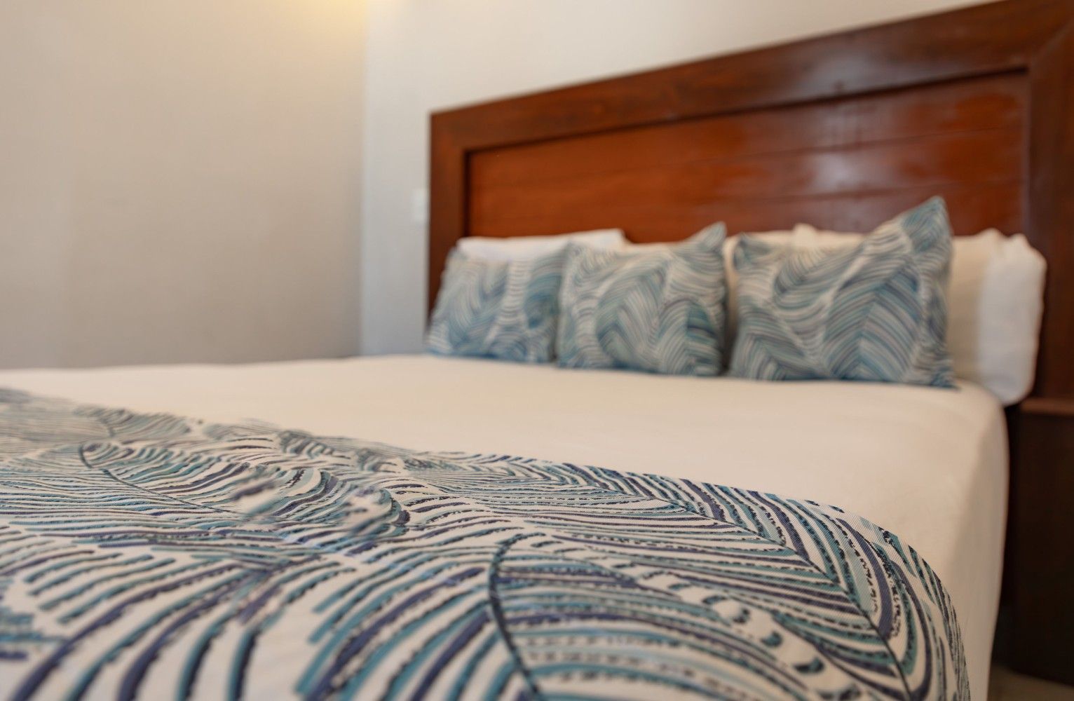 Cama bien hecha con ropa de cama estampada en azul y cabecero de madera en un dormitorio con iluminación tenue.