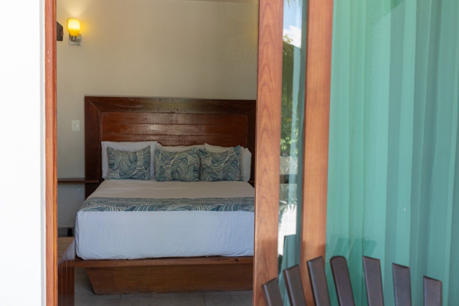 Acogedora habitación con cama de madera, cojines estampados y cortinas turquesas que dan a un balcón.