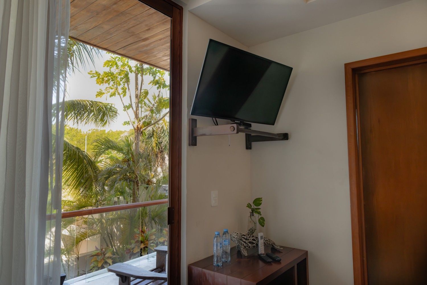 Televisor montado en la pared sobre una mesita en una habitación luminosa junto a una ventana abierta.