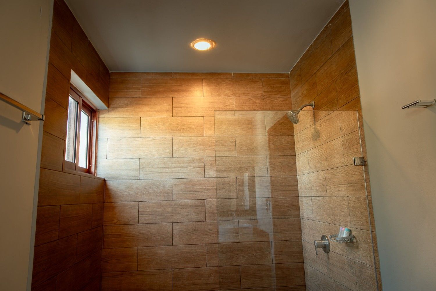 Ducha vacía con azulejos, paredes revestidas de madera, ventana y luz en el techo.
