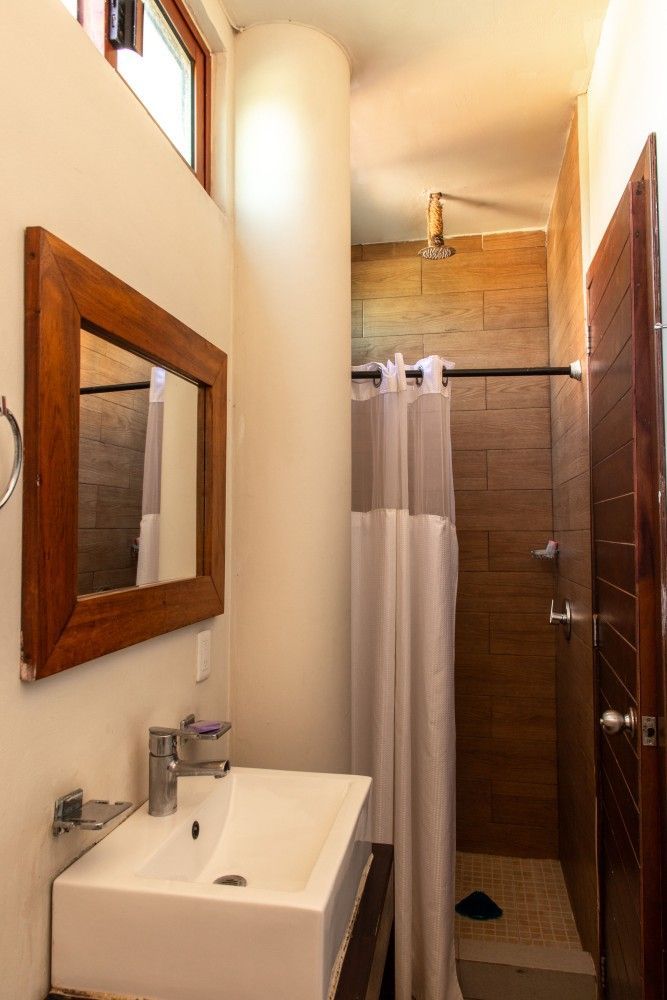 Baño estrecho con lavabo, espejo, cortina de ducha y paredes de azulejos beige.