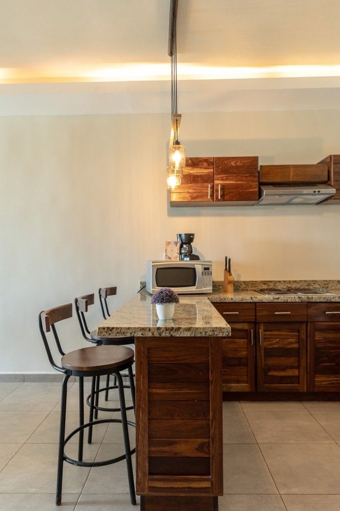 Cocina moderna con isla de granito, dos taburetes de bar, armarios de madera y lámparas colgantes.