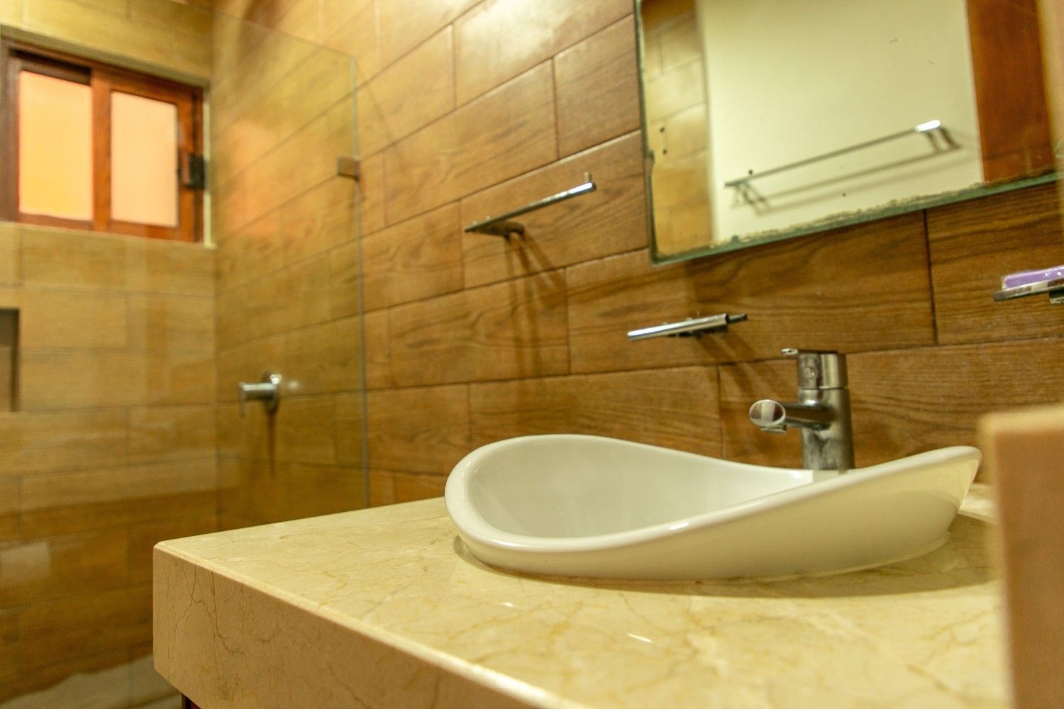 Baño moderno con azulejos beige, lavabo blanco sobre encimera y espejo sobre grifo cromado.