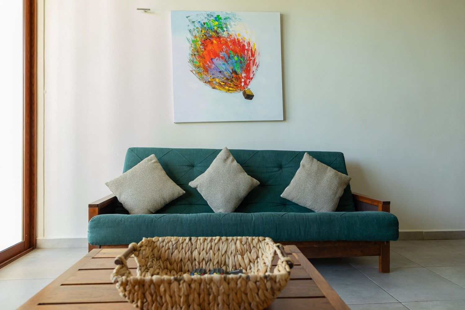 Sala de estar moderna con sofá color turquesa, cojines beige, arte abstracto en la pared y una mesa de centro tejida.