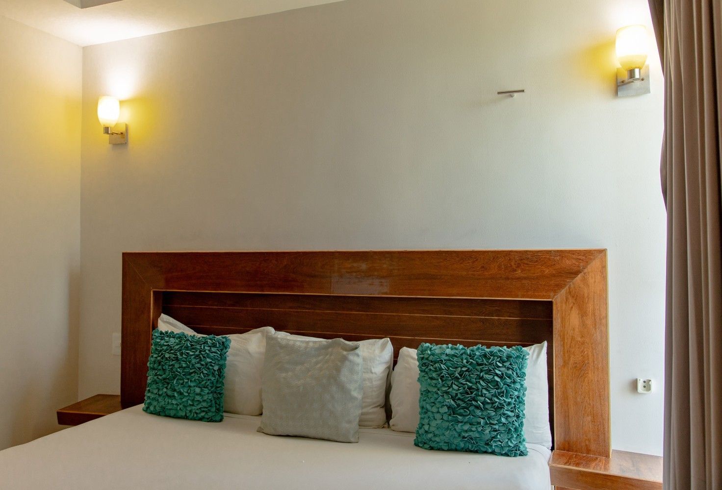 Dormitorio moderno con cabecero de madera, ropa de cama blanca y cojines decorativos de color turquesa.
