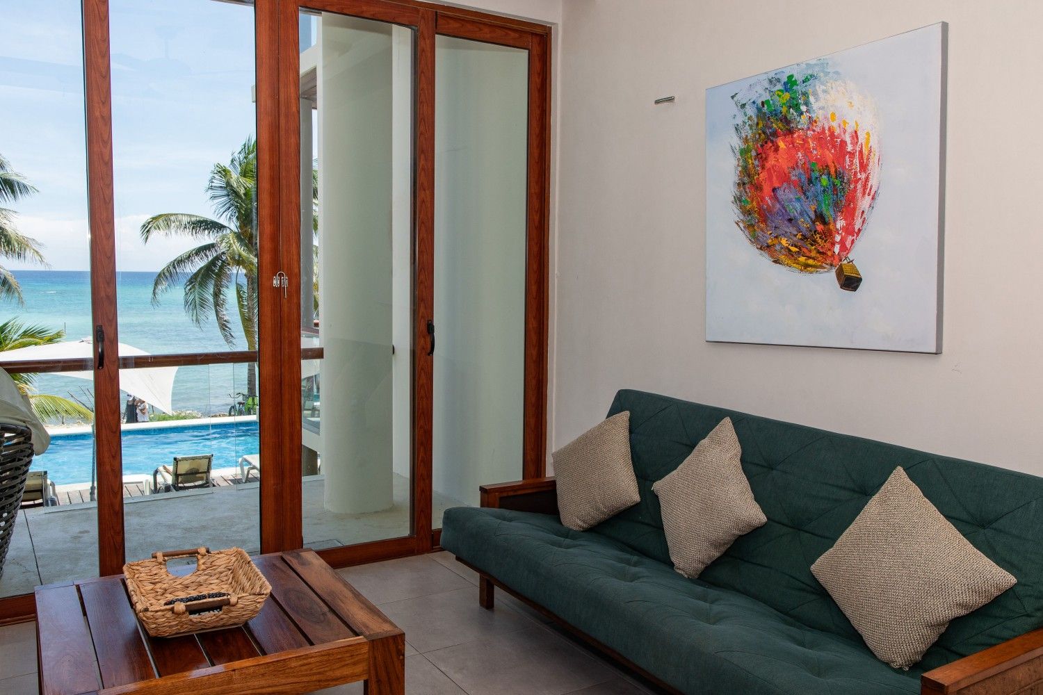 Acogedora sala de estar con sofá verde, arte abstracto en la pared y puertas que dan a un balcón con vistas al océano.