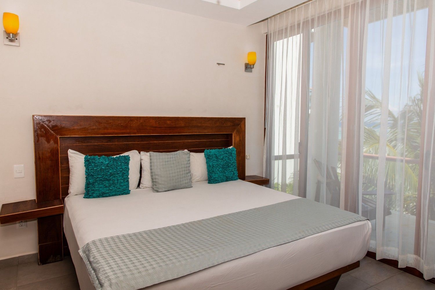 Habitación luminosa con cama king size, almohadas color turquesa y cortinas que van del suelo al techo junto a la ventana.