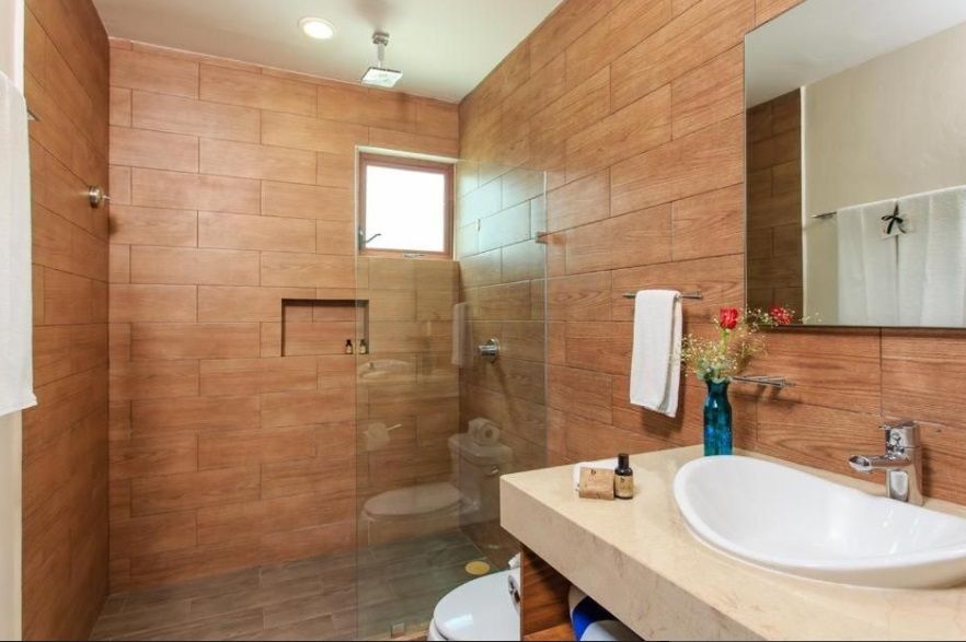 Baño moderno con azulejos color beige, ducha de cristal, lavabo con tocador y luz de ventana.