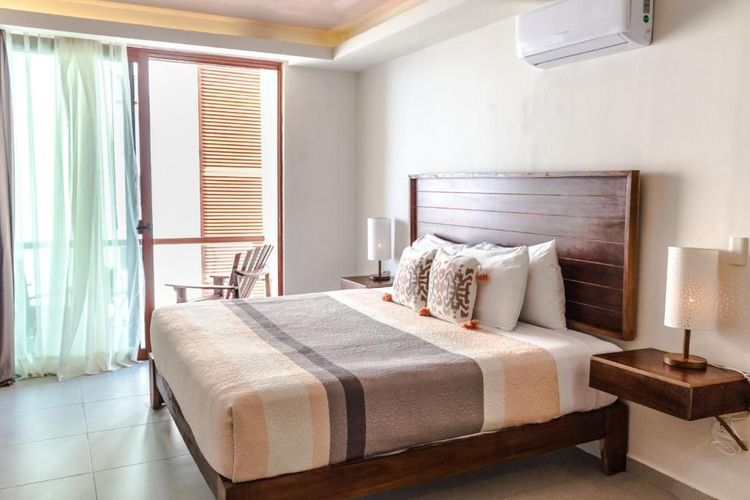 Habitación luminosa con cama king size, cabecero de madera, cortinas suaves y luz de balcón.