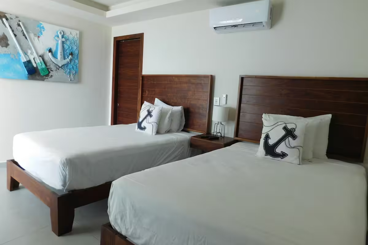 Habitación de hotel con dos camas individuales, sábanas blancas, cuadros en las paredes y aire acondicionado.