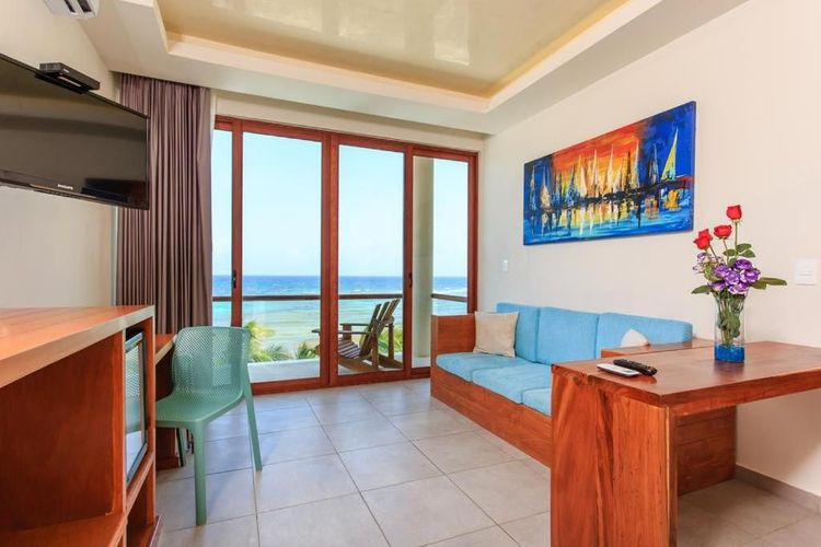 Luminoso salón con vistas al mar, sofá azul, mesa de madera y puertas correderas de cristal que dan a un balcón.