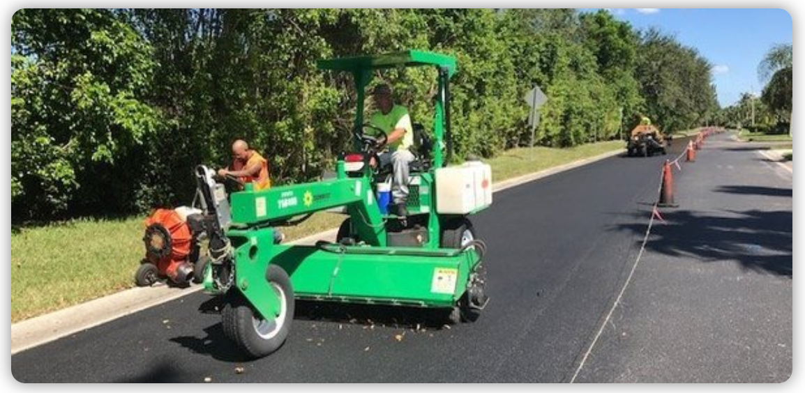 A green machine is laying asphalt on the side of a road.
