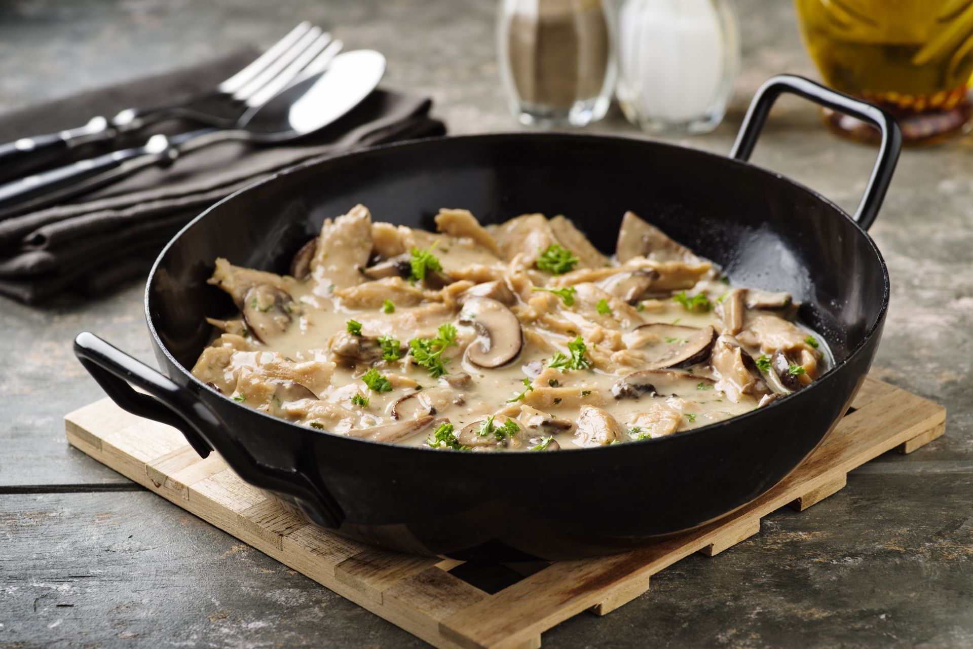 Hähnchen-Pilz-Stroganoff in einer schwarzen Pfanne, serviert mit Silberbesteck.
