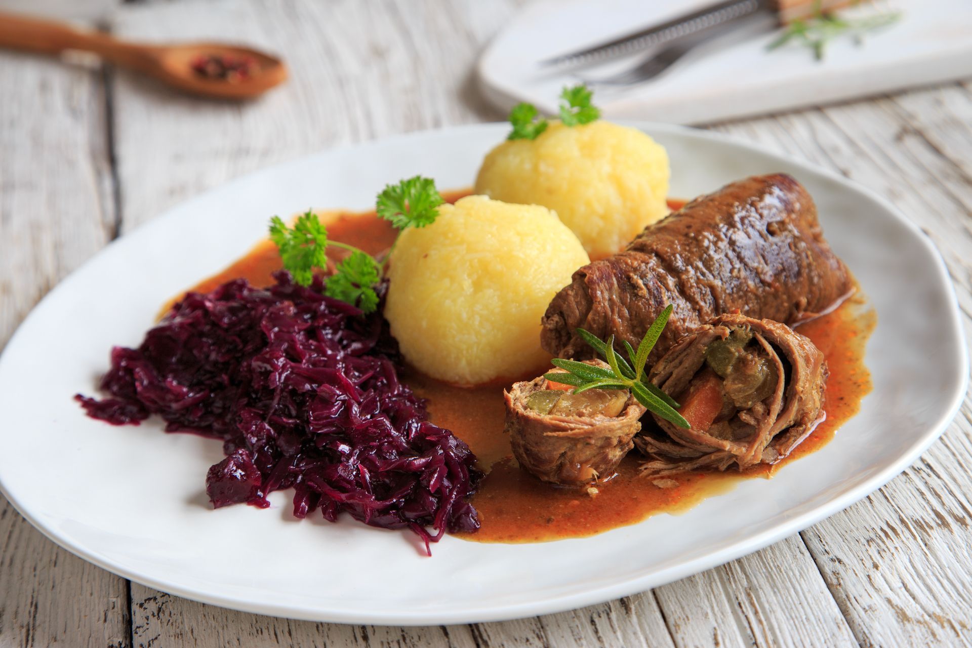 Teller mit Rinderroulade, Kartoffelknödeln und Rotkohl in Soße.