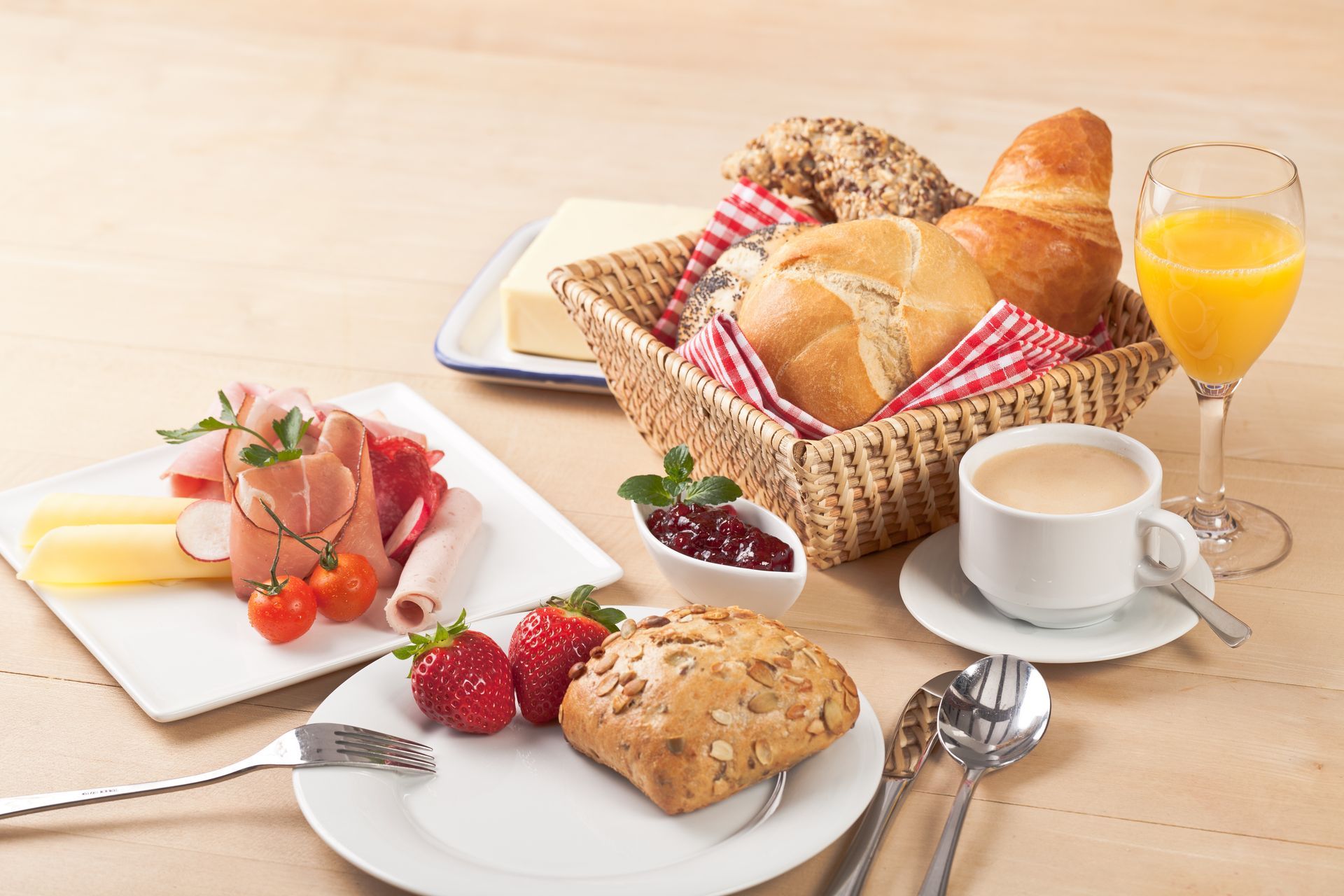 Frühstücksbuffet: Brot, Gebäck, Obst, Kaffee, Fleisch und Saft auf einem Holztisch.