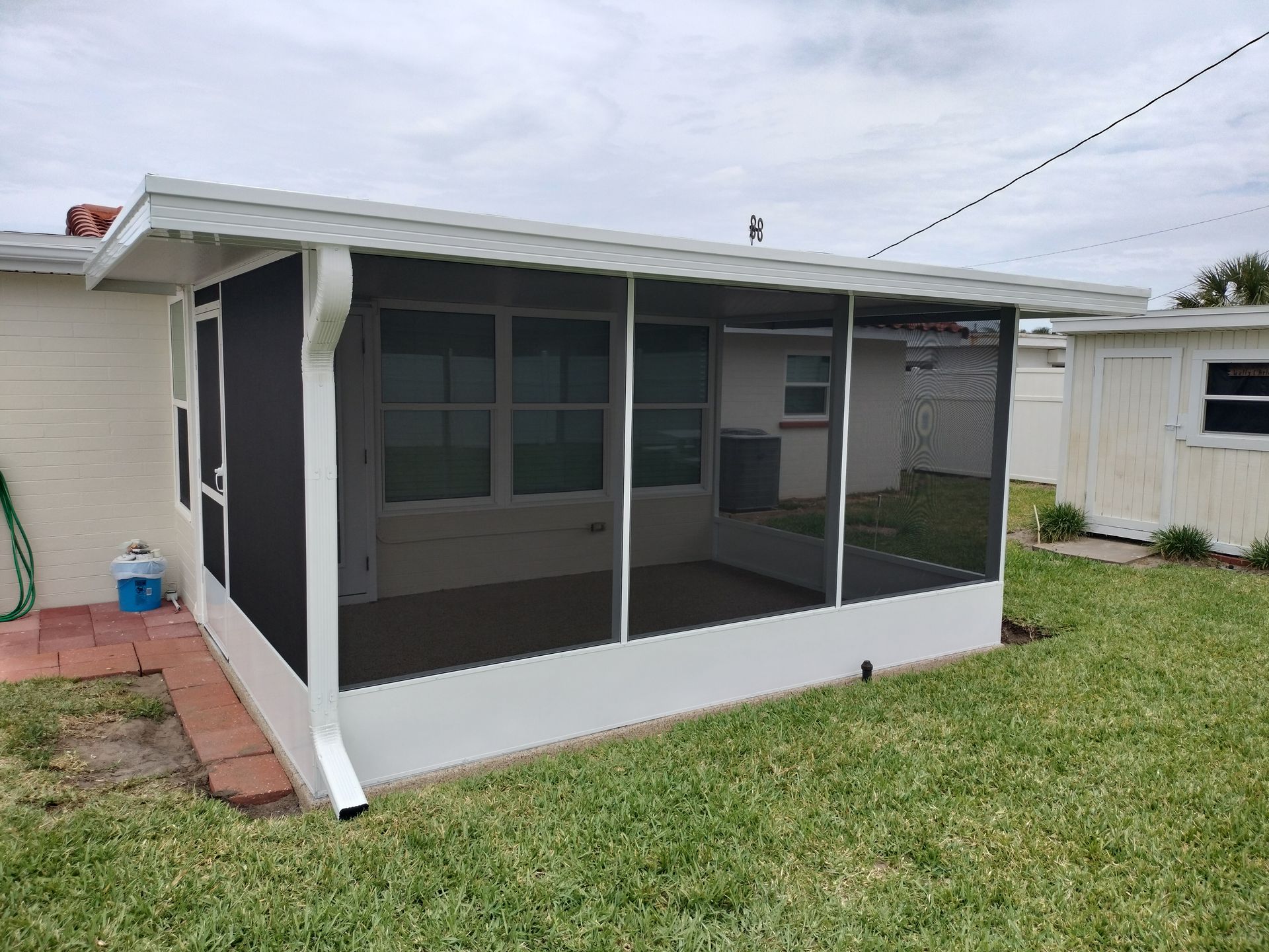Screened-in porch with black trim and white base on a grassy backyard patio
