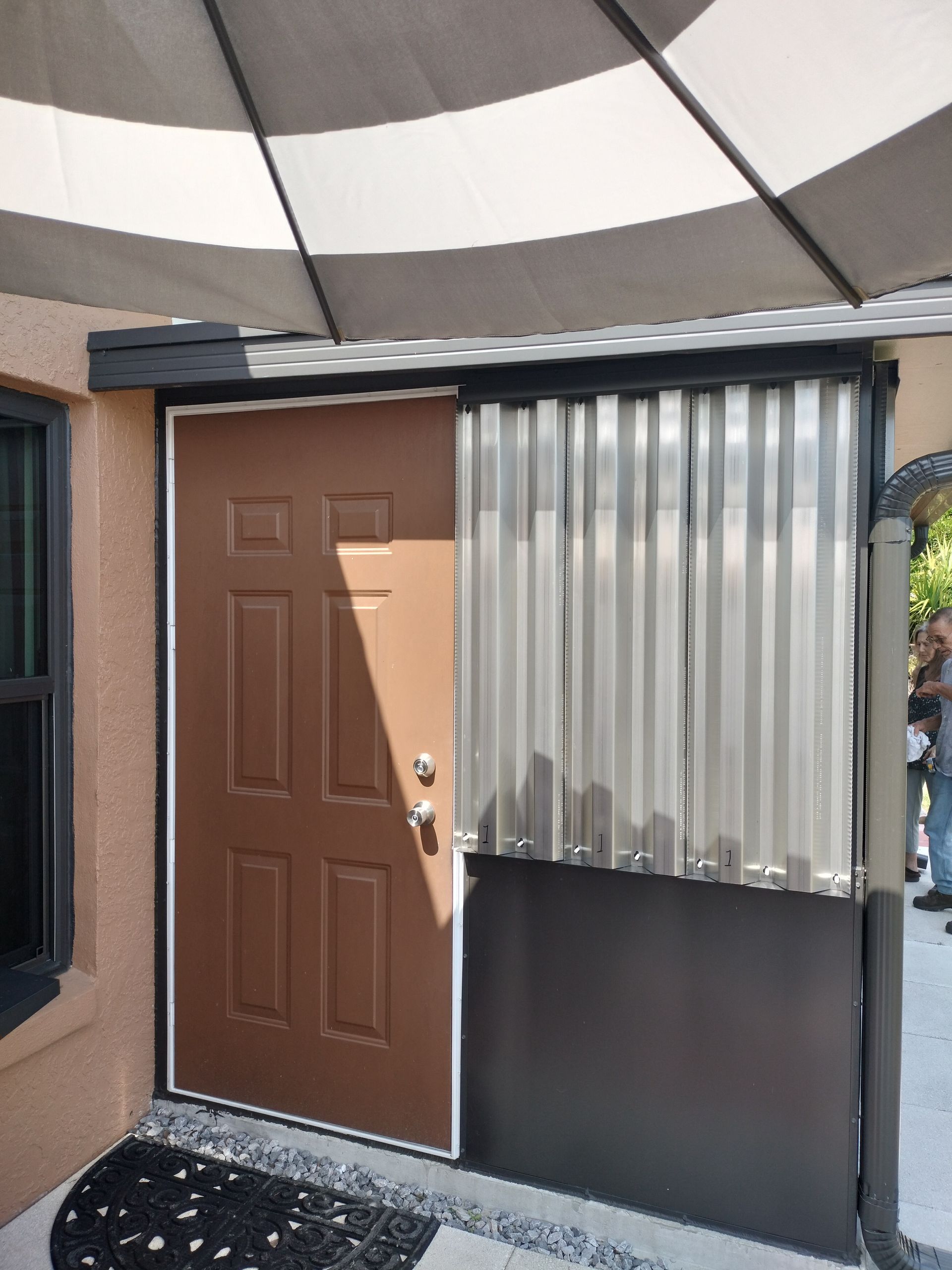 Brown door and window on a small curved porch with translucent paneling and a striped awning