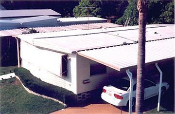 A white car is parked under a canopy in front of a house