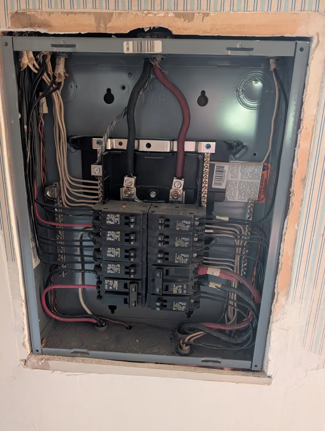 Open electrical breaker panel with wiring and circuit breakers exposed in a wall recess